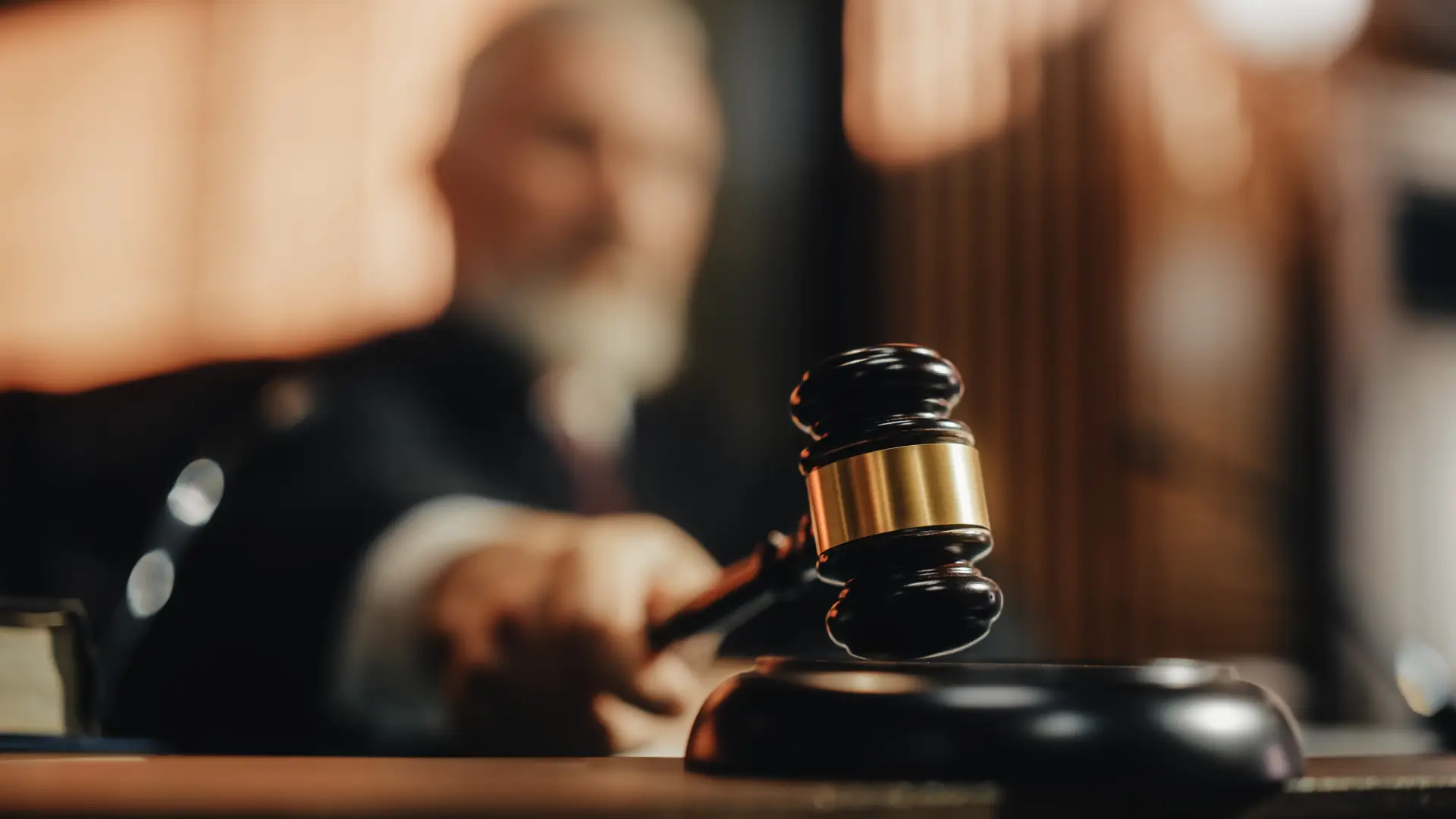 A judge blurred in the background pounds a gavel in the focused foreground