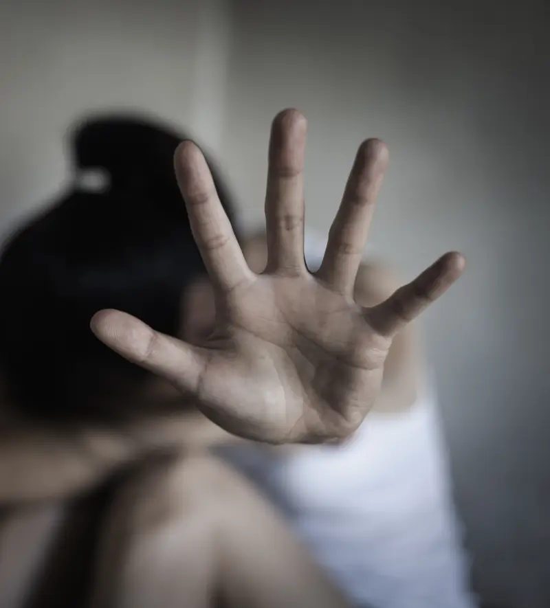 A woman sitting on the floor with her head in her arm and knees, while the other arm is extended holding up a hand to say: stop