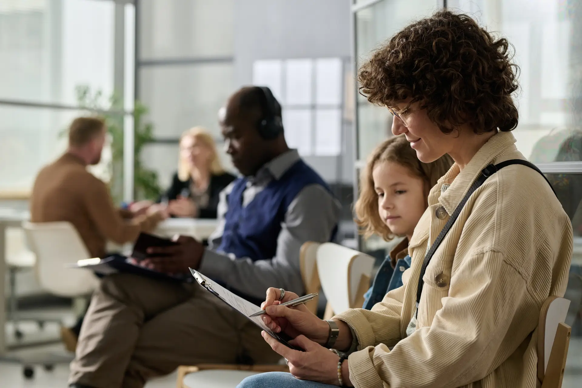 A parent fills out a form in waiting chair next to their child