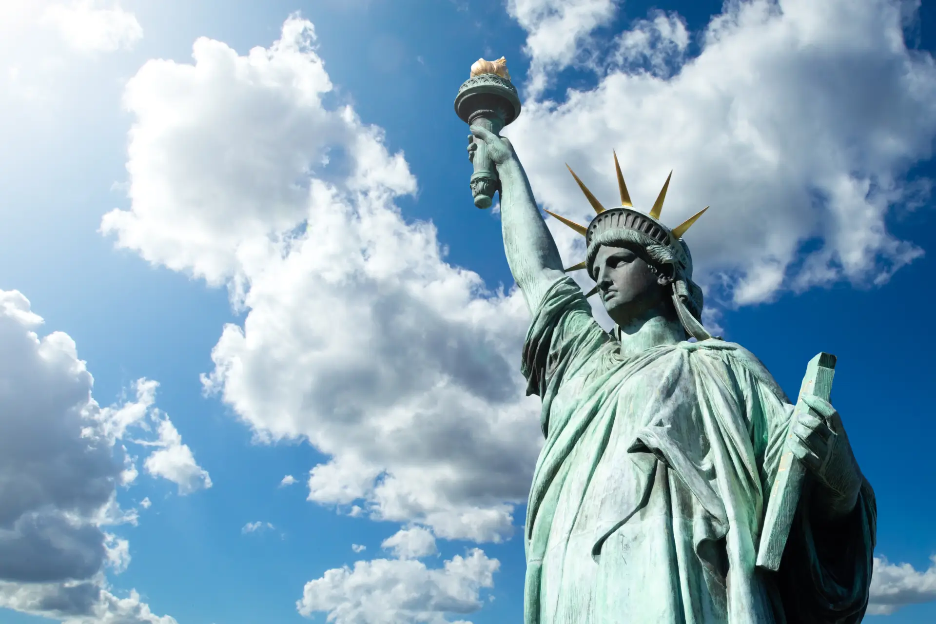 Statue of liberty in the foreground of a blue cloudy sky
