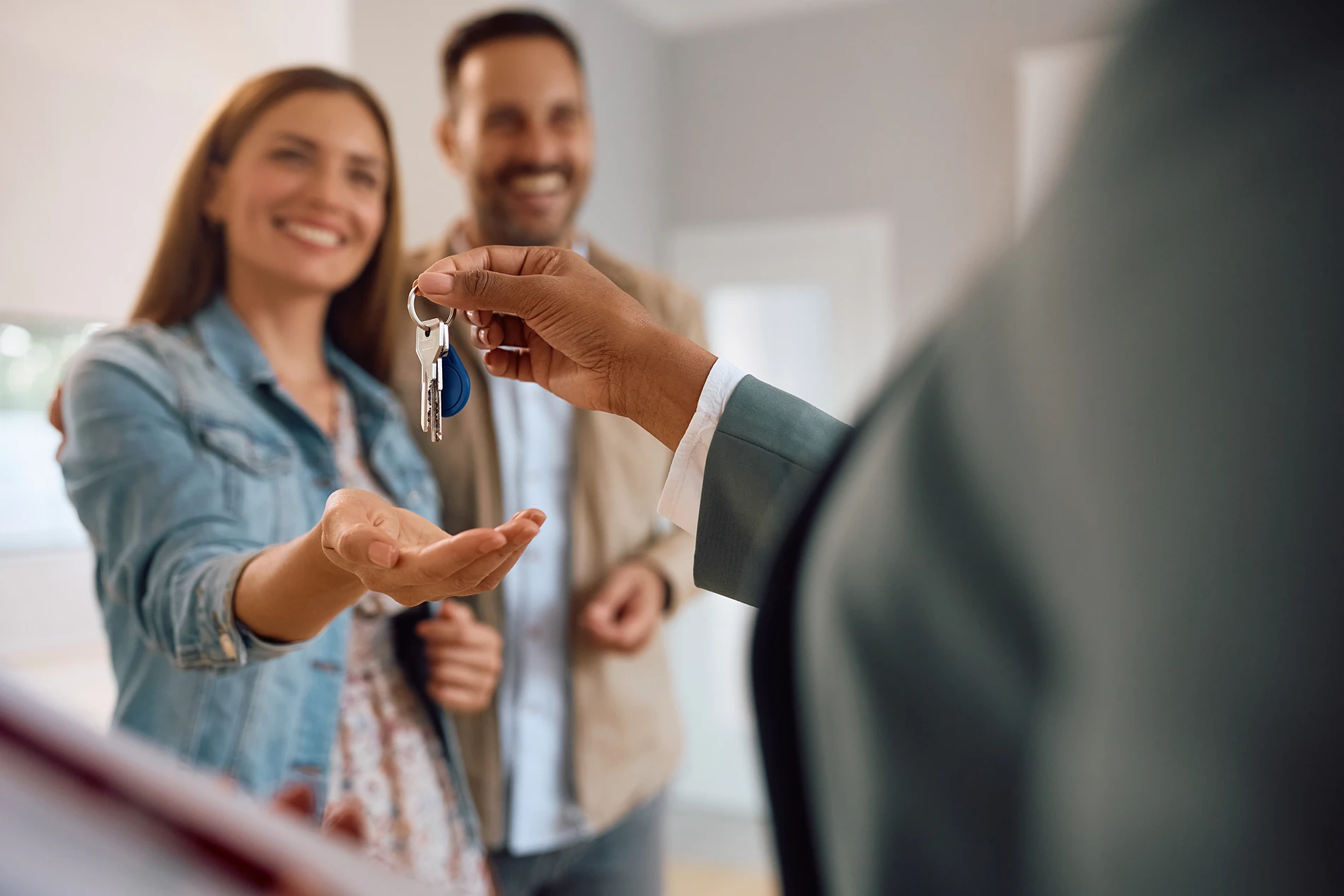 A couple stands smiling, reaching out to receive keys from a person in a suit