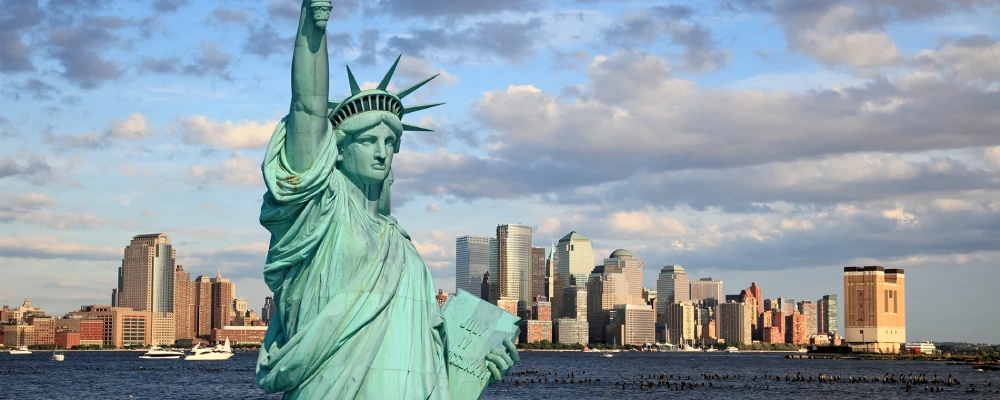 Statue of liberty in the foreground of a blue cloudy sky